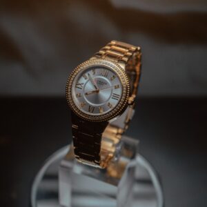 Stylish gold wristwatch showcased on a reflective stand with a dark background.